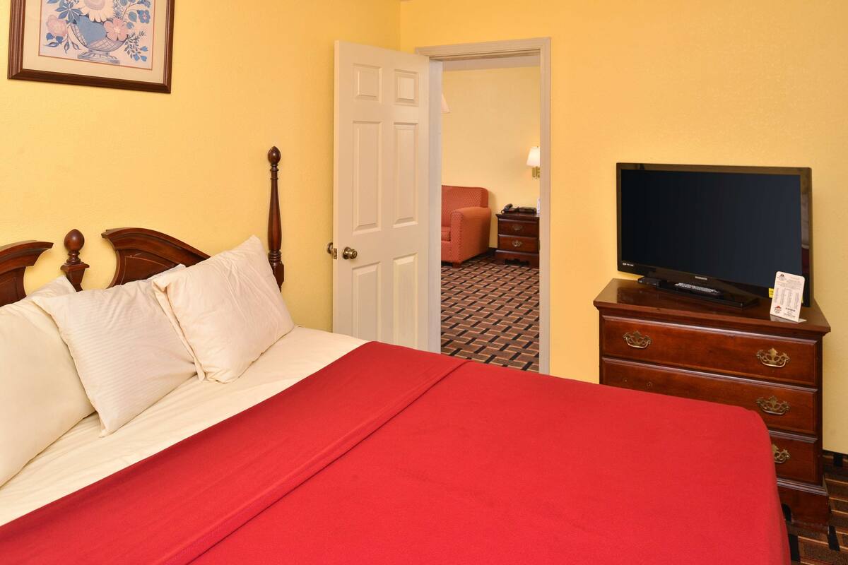 A hotel room with a bed, a television on a dresser, and a door leading to another room.
