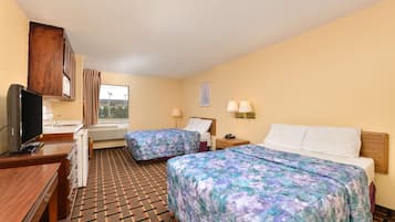 A hotel room with two beds, a desk with a TV, a window with curtains, and a patterned carpet.