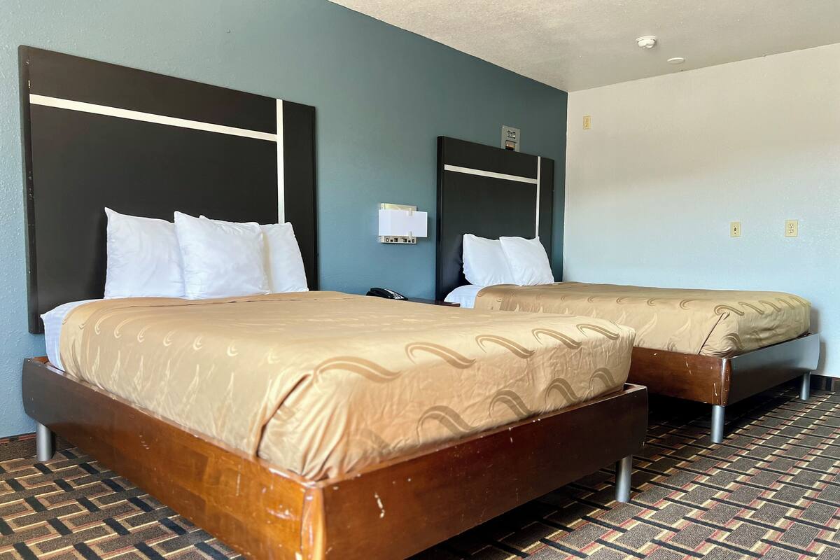 A hotel room with two beds, a patterned carpet, and a modern design.