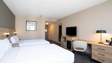 A hotel room with two beds, a desk, a chair, a television, and a desk lamp.