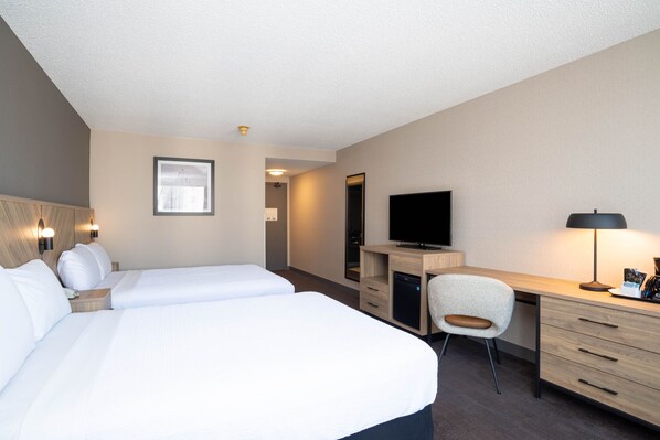 A hotel room with two beds, a desk, a chair, a television, and a desk lamp. - Sandman Hotel Montreal - Longueuil (Longueuil)