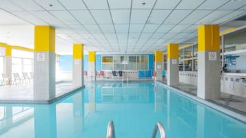 An indoor swimming pool with clear water, yellow and white pillars, and a tiled ceiling.