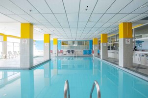 An indoor swimming pool with clear water, yellow and white pillars, and a tiled ceiling.