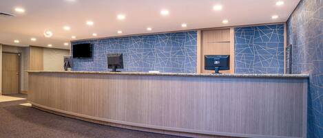 A reception area with a curved counter, a flat-screen TV, and a digital display.