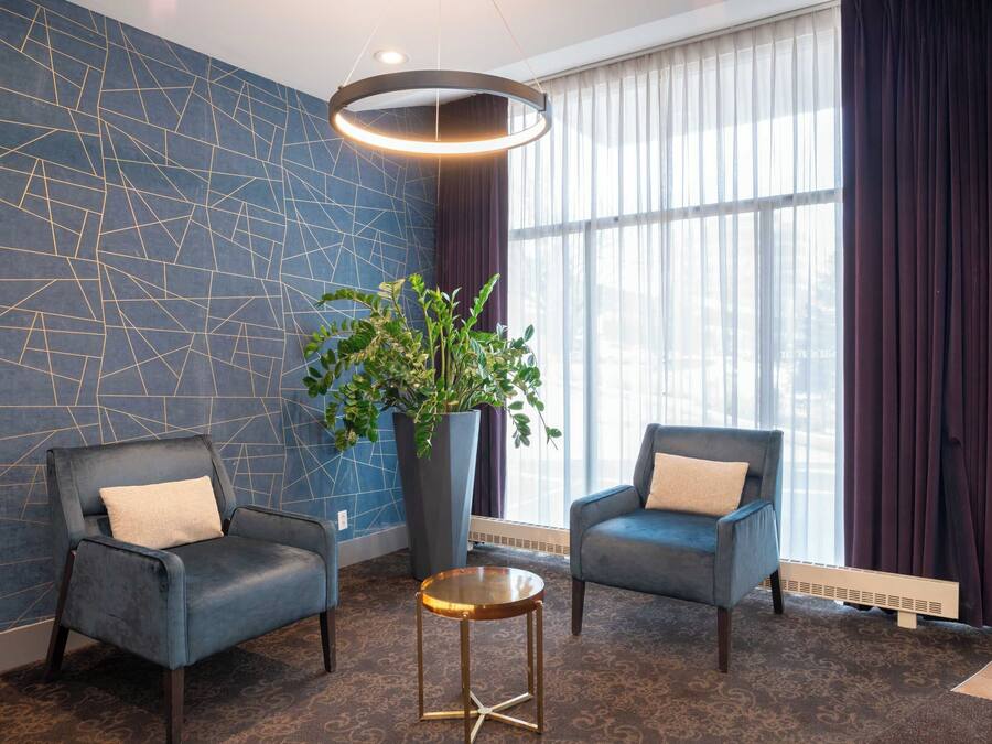 Una habitación moderna con dos sillones, una planta grande en maceta y una mesa redonda.