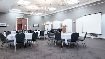 A conference room with round tables, black chairs, a whiteboard, and a projector screen.