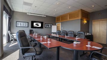 Uma sala de conferências com uma mesa comprida, várias cadeiras e uma tela de projetor.