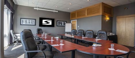A conference room with a long table, multiple chairs, and a projector screen.