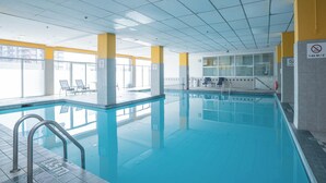 An indoor swimming pool with clear glass walls, a tiled floor, and a ceiling with a grid pattern.