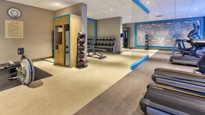 Een sportschool met loopbanden, gewichten en een roeiapparaat.