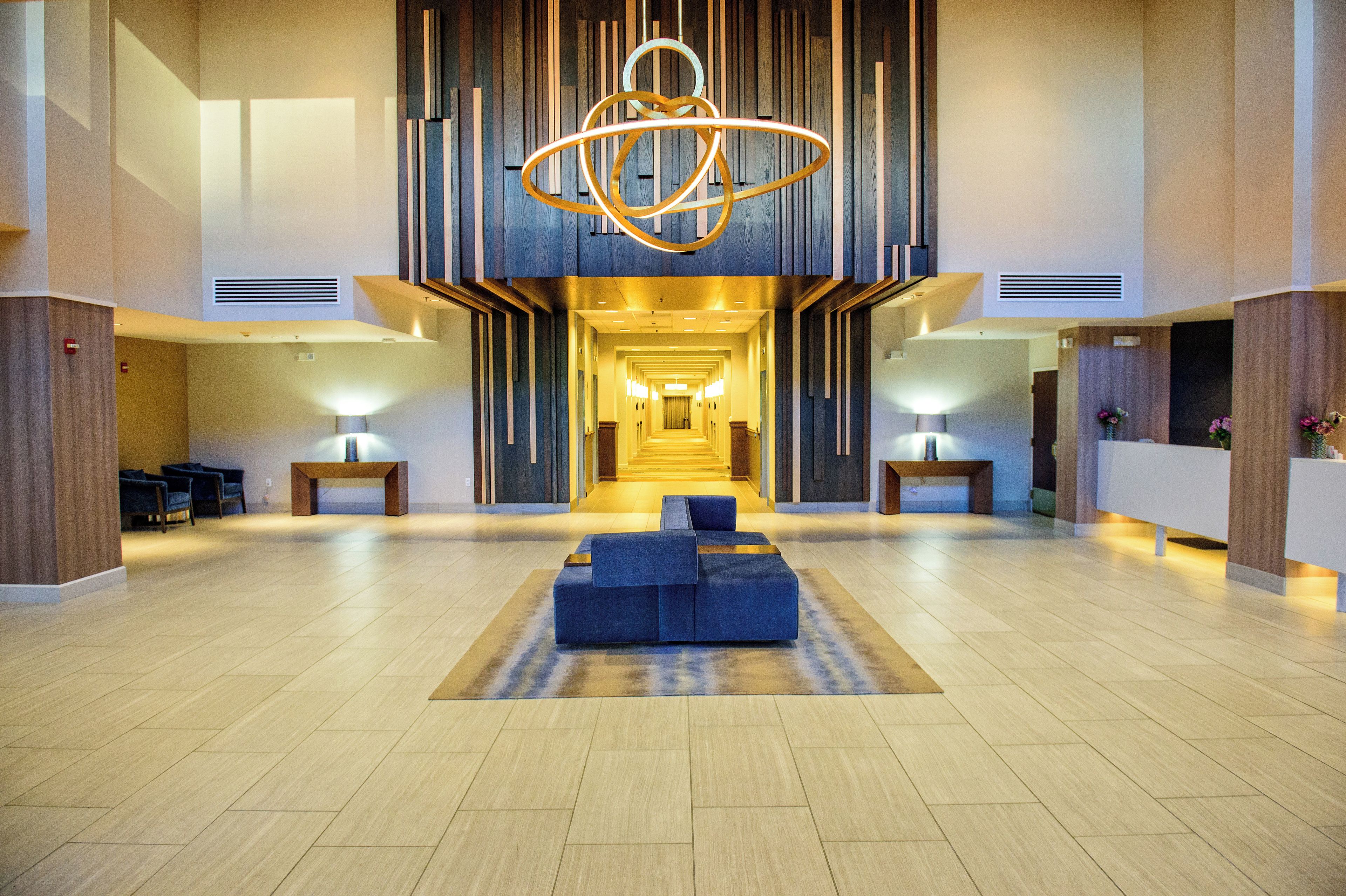 A hotel lobby with a central seating area, a staircase leading to upper floors, and a modern chandelier.