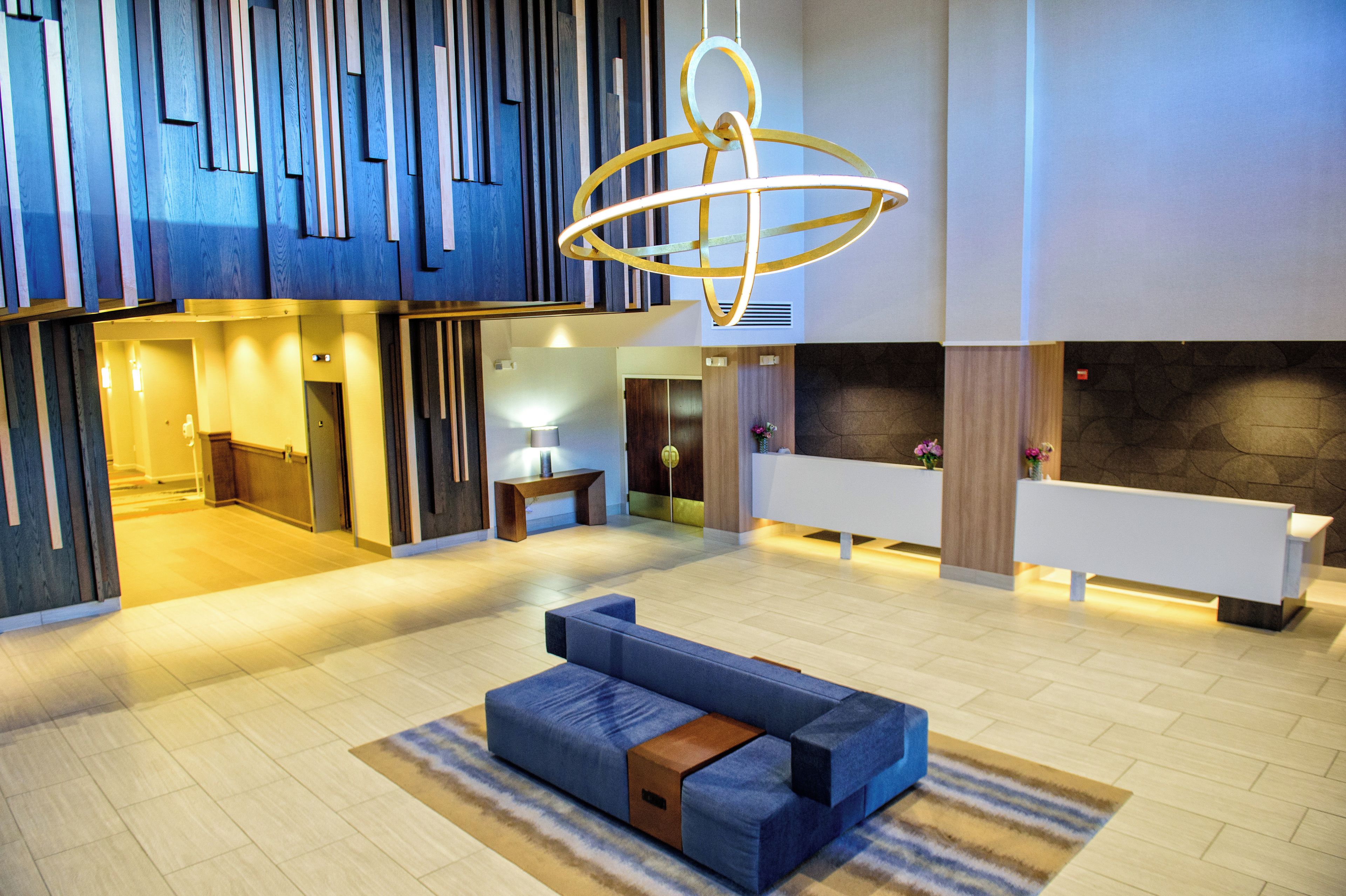 Eine moderne Lobby mit einer Rezeption, einer Sitzgelegenheit und einer außergewöhnlichen Deckenleuchte.