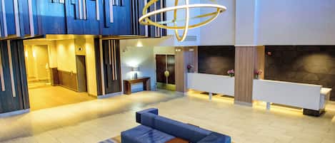 A modern lobby with a reception desk, seating area, and a unique ceiling light fixture.