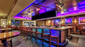 A modern bar area with wooden bar counters and chairs, a large screen, and artwork on the walls. - Crowne Plaza Dulles Airport by IHG (Herndon)