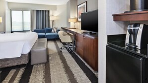 Een hotelkamer met een bed, een bank, een bureau met een televisie, een koffieapparaat en een groot raam.
