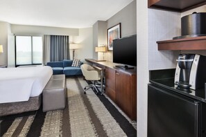 Une chambre d’hôtel comprenant un lit, un canapé, un bureau avec une télévision, une machine à café et une grande fenêtre.