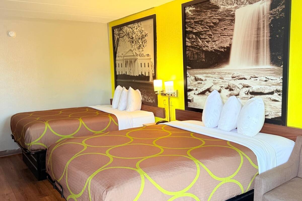 Ein Hotelzimmer mit zwei Betten, einem großen Wandbild und einem Nachttisch mit Lampe.