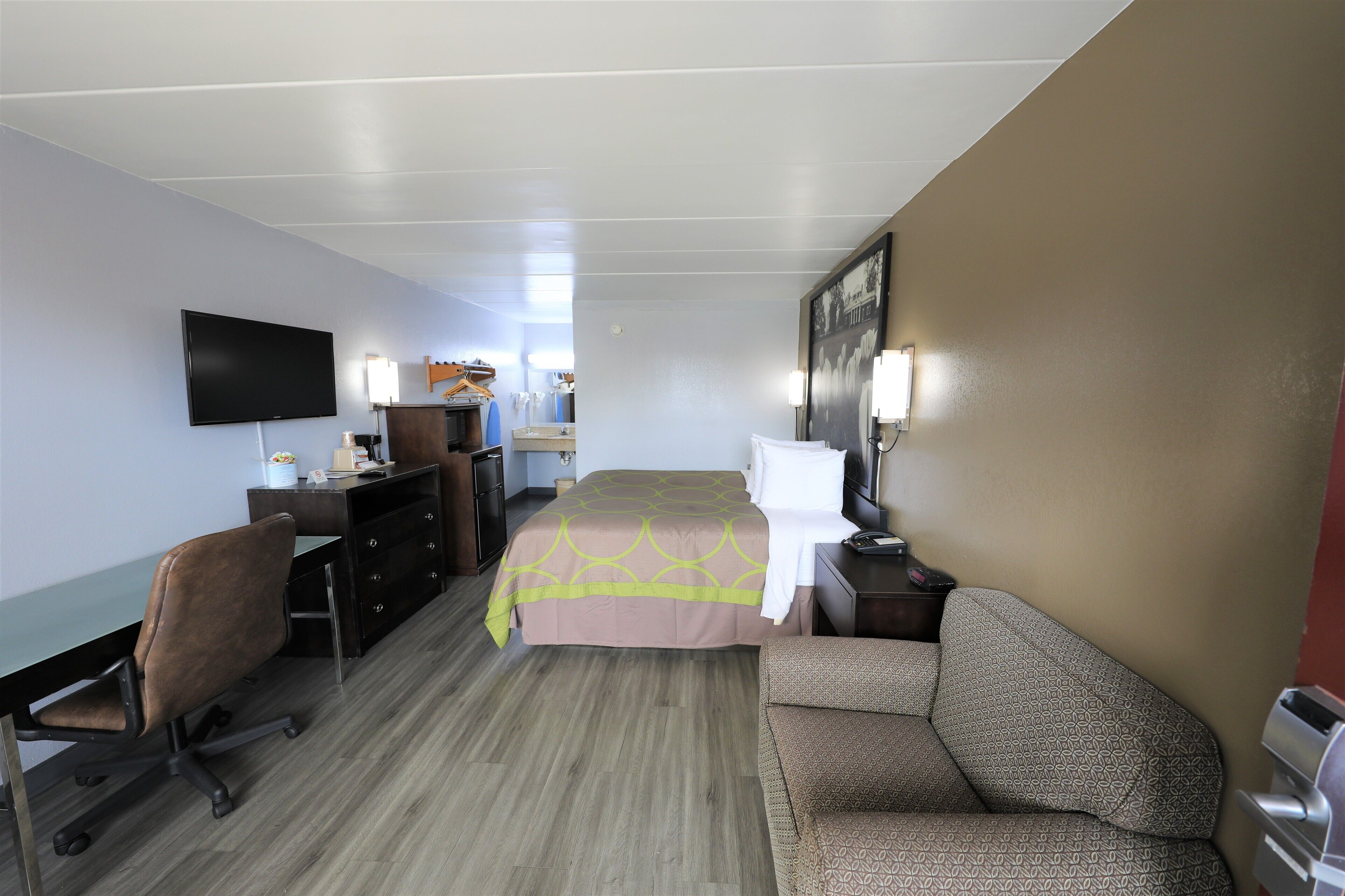 A hotel room with a bed, a desk, a chair, a TV, and a dresser.