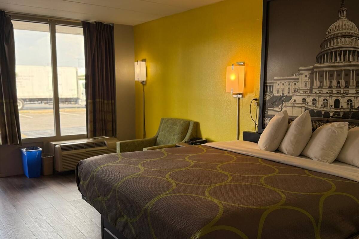 Ein Hotelzimmer mit einem großen Bett, einem Sessel, einem Schreibtisch und einem Fenster mit Vorhängen.