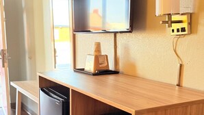 Una kitchenette compacta con refrigerador incorporado, microondas y un televisor pequeño sobre una encimera de madera.