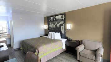 A hotel room with a bed, a chair, a desk, and a wall-mounted lamp.