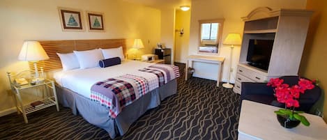 A hotel room with a bed, bedside tables, a desk, a TV, and a flower vase.