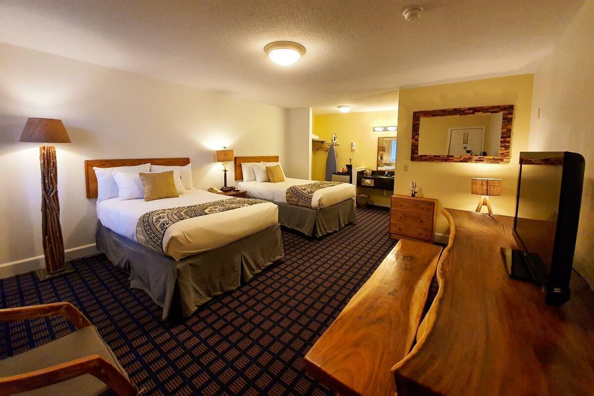 Habitación de hotel con dos camas, un banco de madera, un escritorio, un espejo y una alfombra estampada.