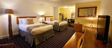 Habitación de hotel con dos camas, un banco de madera, un escritorio, un espejo y una alfombra estampada.