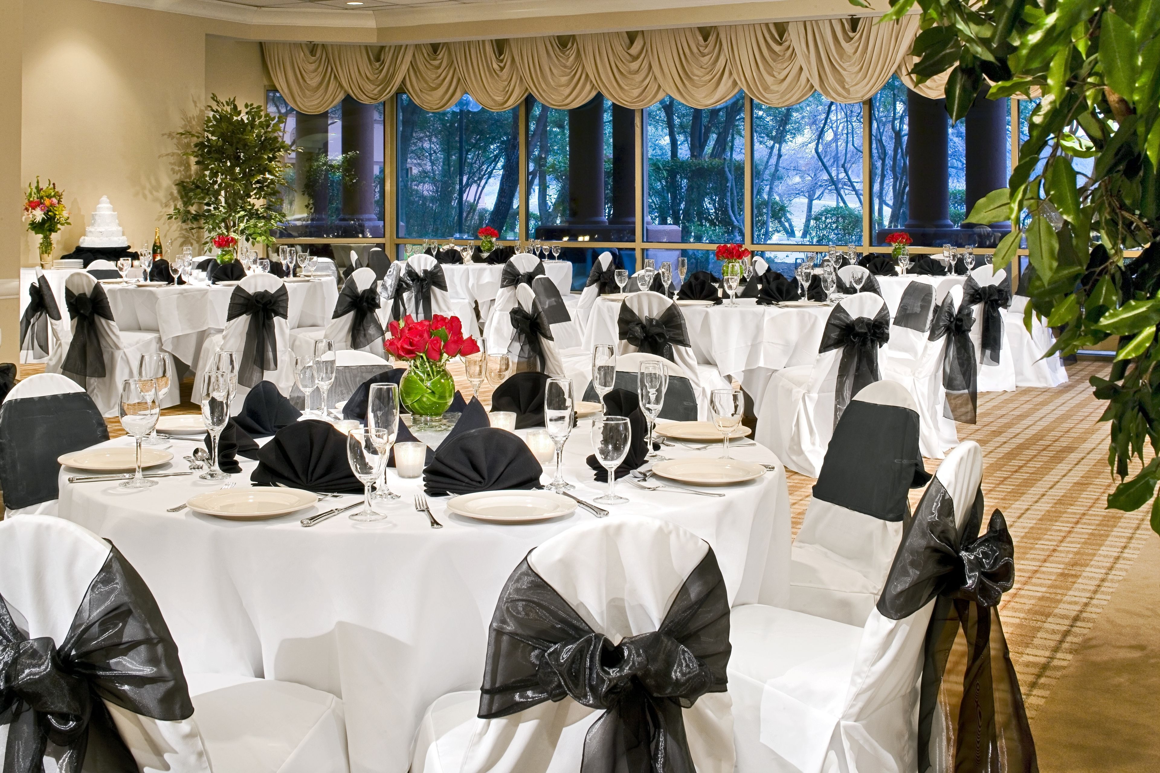 A banquet hall with round tables, black and white tablecloths, and chairs with black bows.
