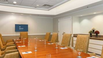 A conference room with a long wooden table, beige chairs, and a flat-screen TV on the wall.