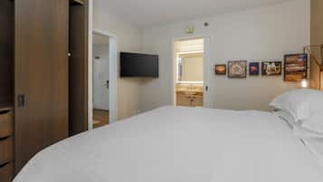 A bedroom with a large bed, a wooden wardrobe, a television mounted on the wall, and a bathroom visible through an open door.