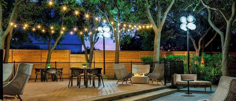 An outdoor patio with wicker furniture, string lights, and a fire feature.
