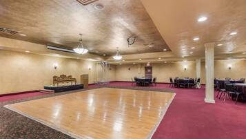 A spacious room with a large wooden dance floor, multiple tables with chairs, and a red carpeted area.