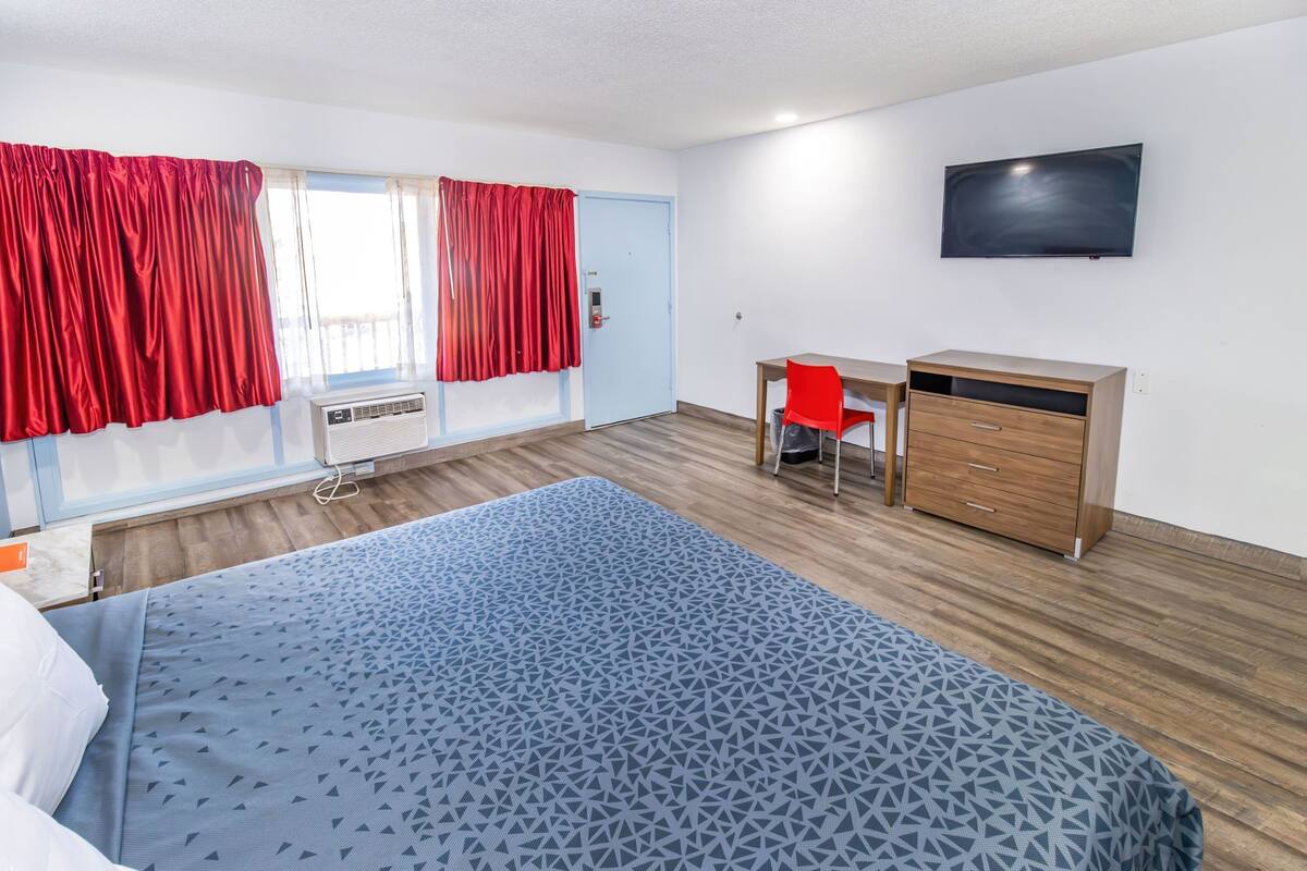Una habitación de hotel con cama, escritorio, silla, televisor y ventana con cortinas.
