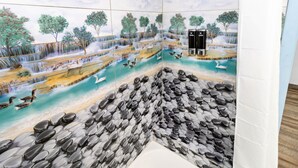 Een badkamer met een muurschildering van een waterval en vogels, een badkuip en een douchegedeelte.