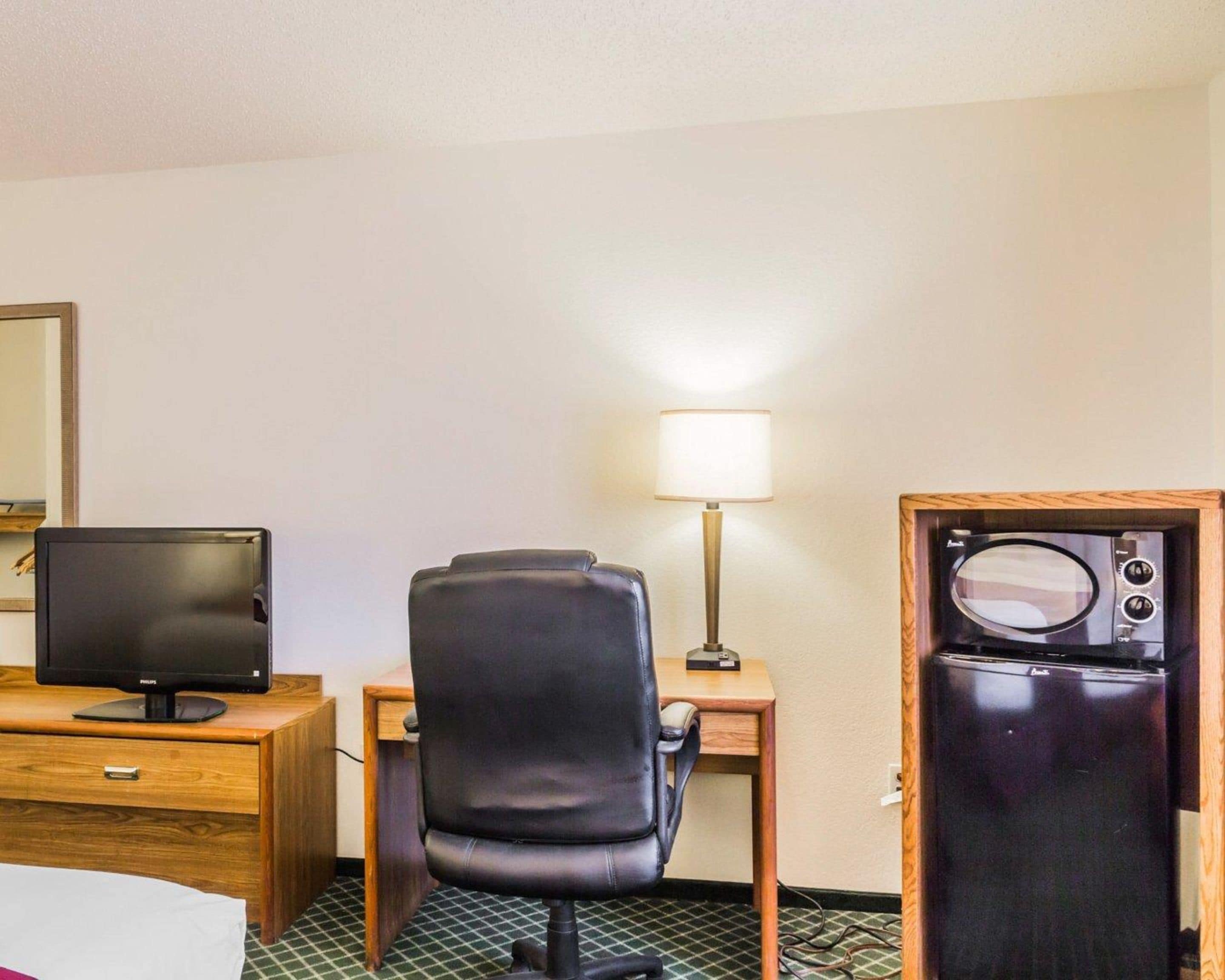 Una habitación de hotel con un escritorio de madera, una silla de cuero negro, un televisor, una lámpara y un refrigerador.