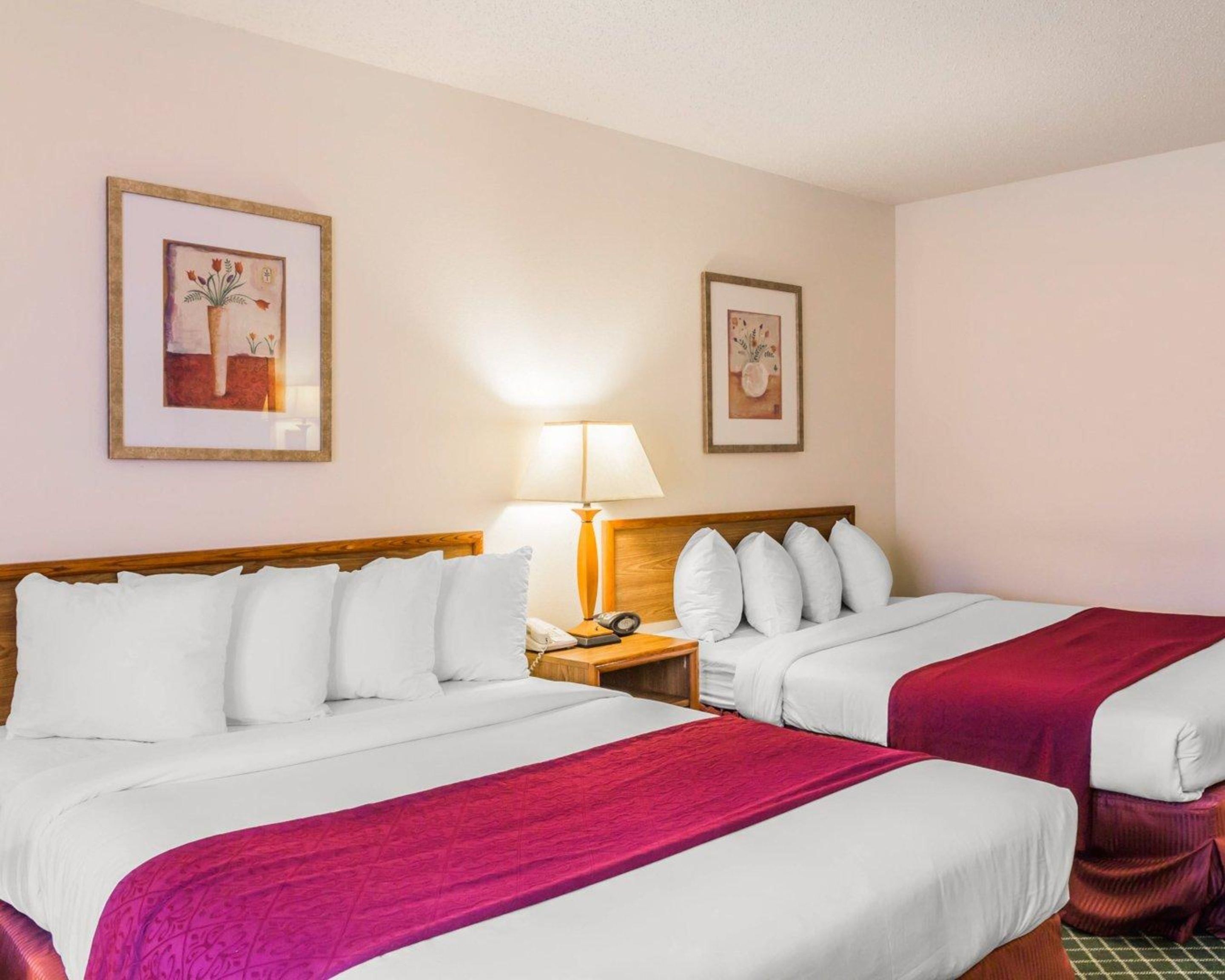 Una habitación de hotel con dos camas, una mesita de noche, una lámpara y dos cuadros en la pared.