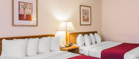 Una habitación de hotel con dos camas, una mesita de noche, una lámpara y dos cuadros en la pared.