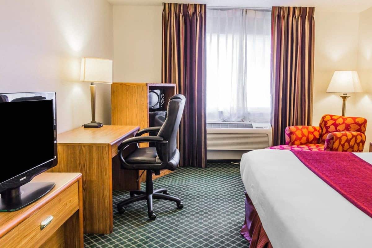 Una camera d'albergo con un letto, una scrivania con un computer, una televisione, una sedia e una finestra con tende.