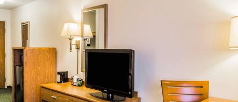 A hotel room with a wooden dresser, a television, a lamp, a mirror, and a chair.