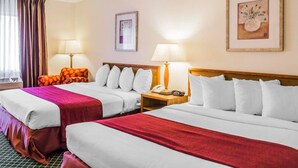 A hotel room with two beds, each with white linens and red throw blankets. There are two bedside tables with lamps, a framed picture on the wall, and a window with curtains. - Quality Inn & Suites Golden - Denver West (Golden)