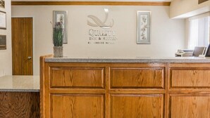 A reception area with a wooden counter, framed artwork, and a sign for 'Quality Inn & Suites by Choice Hotels'. - Quality Inn & Suites Golden - Denver West (Golden)