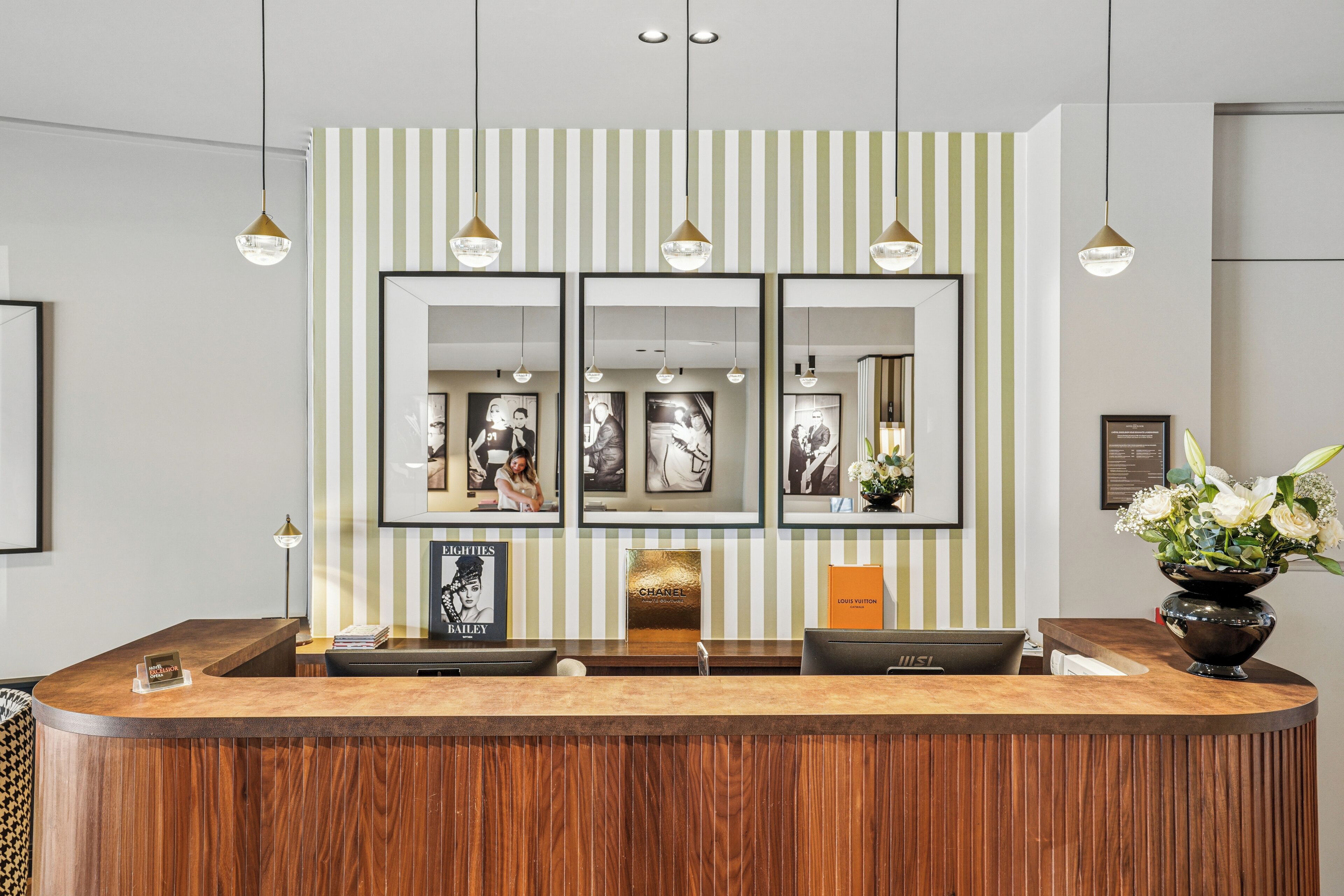 Un comptoir d’accueil avec un revêtement en bois, des photographies encadrées accrochées au mur et un vase rempli de fleurs.