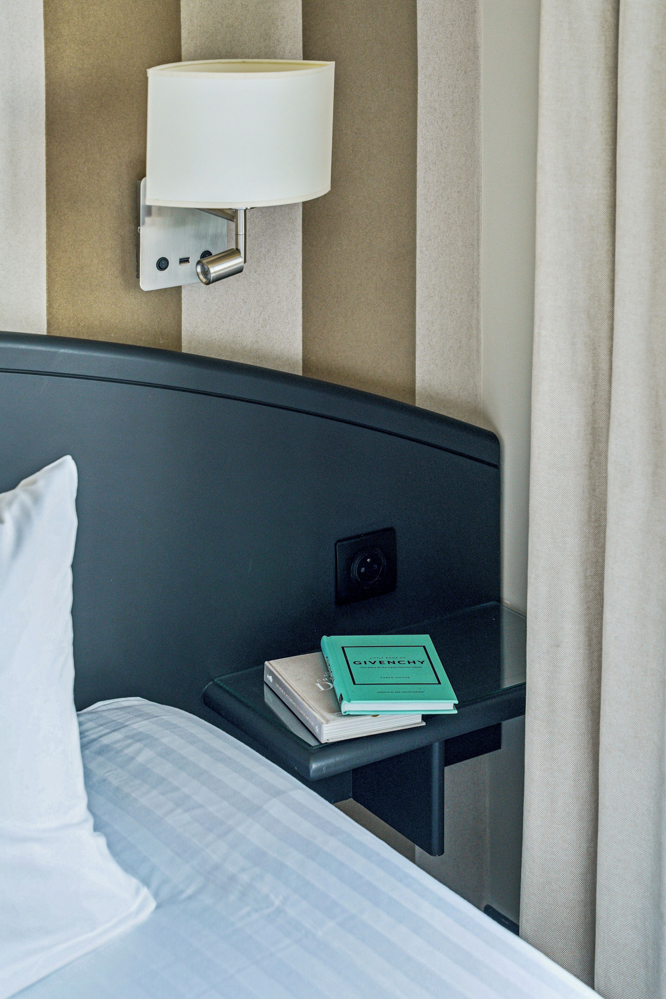 Une chambre d’hôtel avec un lit, une table de chevet avec une lampe, un livre et un luminaire fixé au mur.