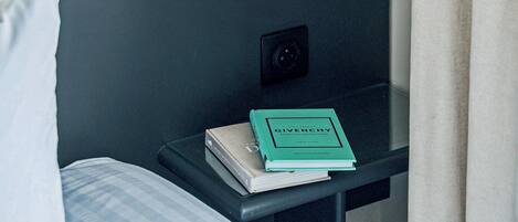 Une chambre d’hôtel avec un lit, une table de chevet avec une lampe, un livre et un luminaire fixé au mur.