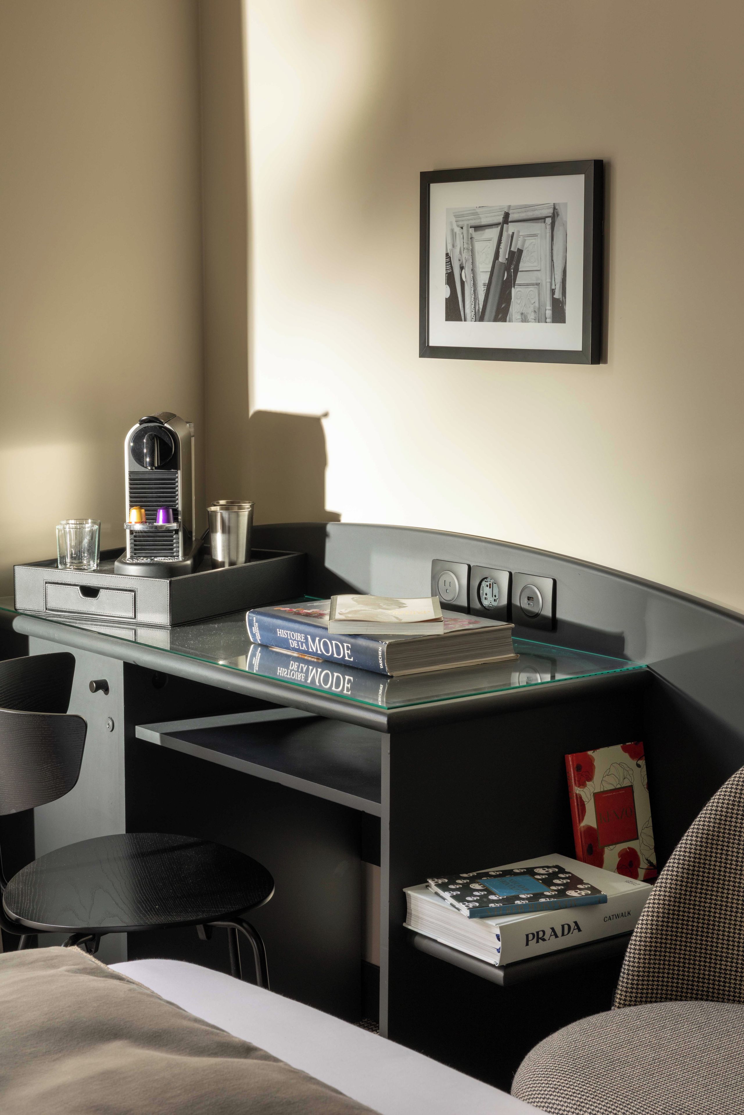 A modern hotel room with a desk, a chair, a bed, and a bookshelf.