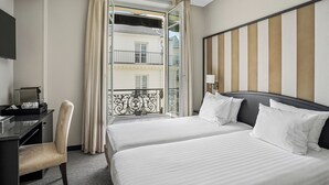 A hotel room with two beds, a desk with a chair, a TV, and a window with curtains. - Hôtel Excelsior Opéra (Paris)
