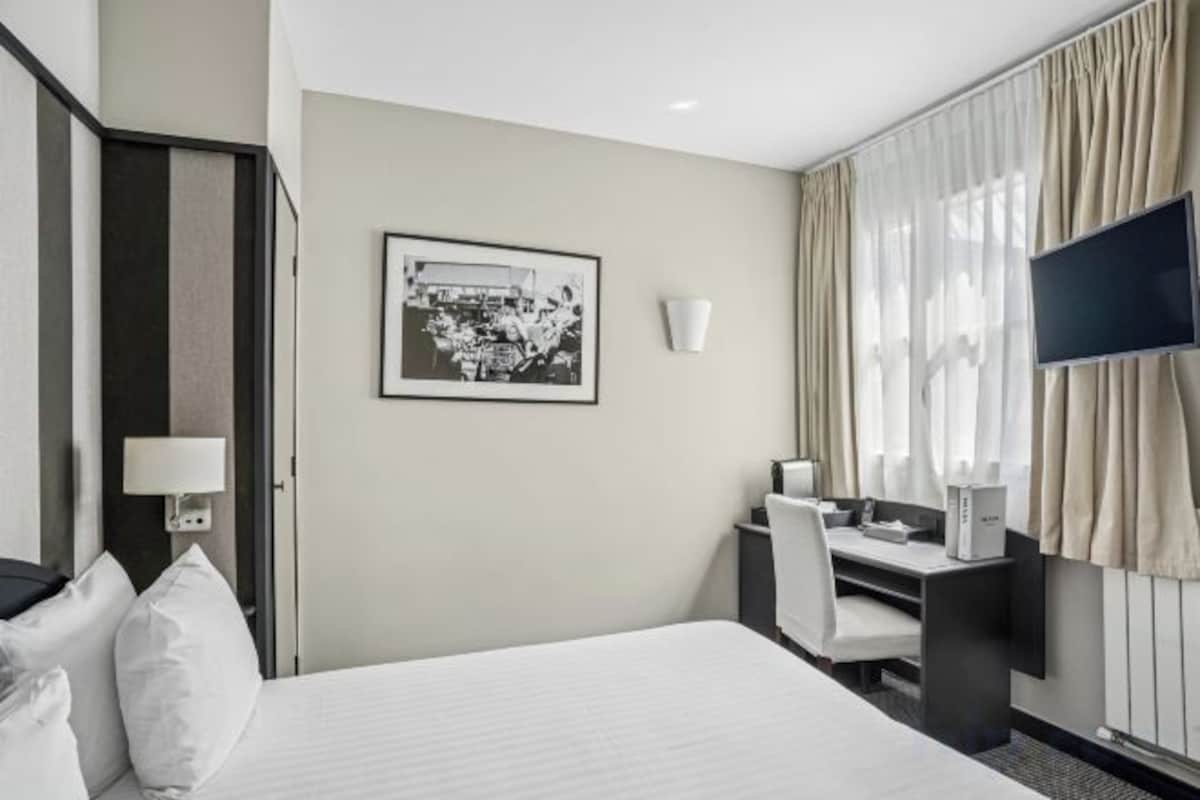 A hotel room with a bed, a desk, a chair, a television, and a window with curtains.