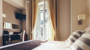 Habitación de hotel con cama, escritorio con una computadora portátil, televisor montado en la pared y ventana con cortinas.