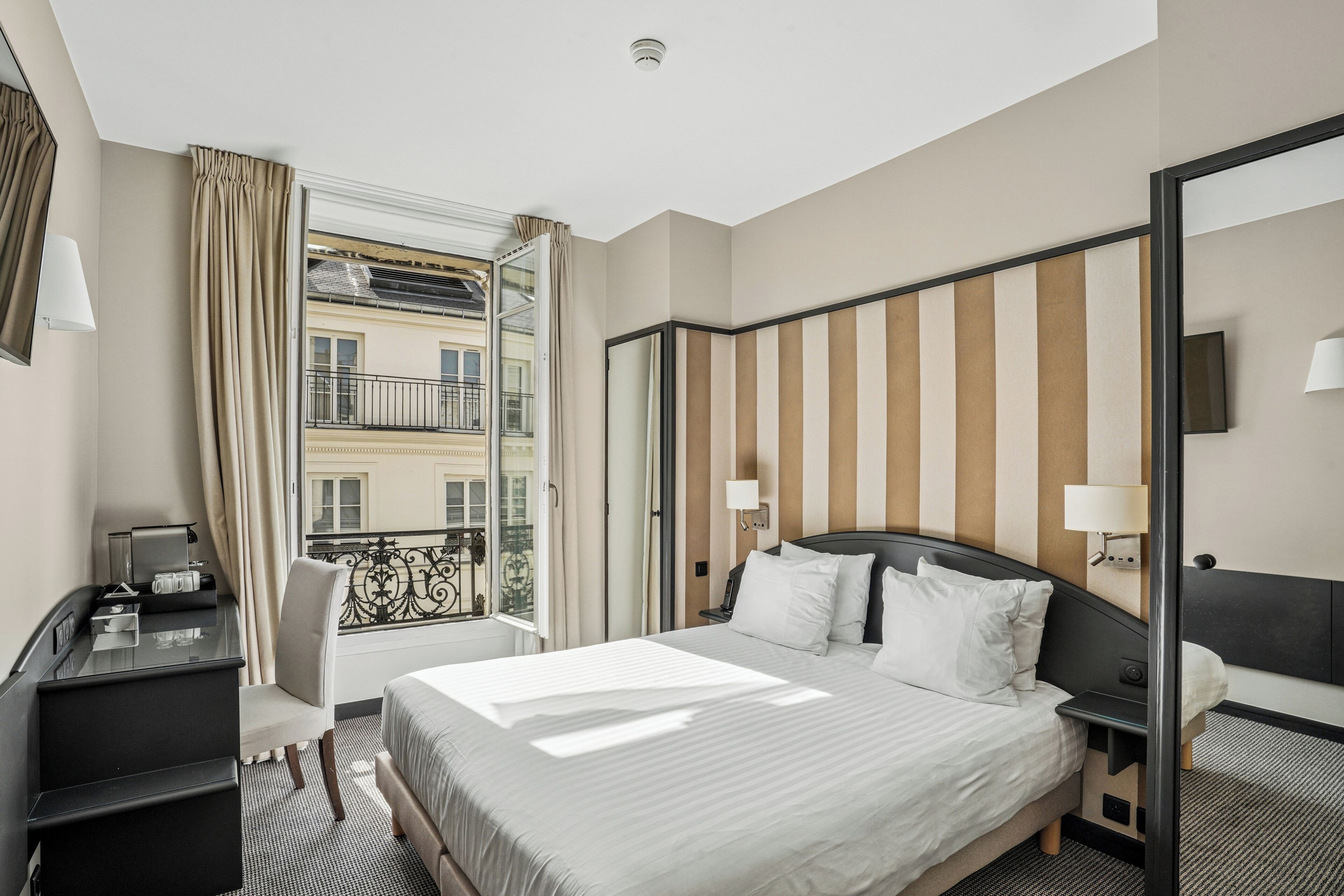 A hotel room with a bed, desk, chair, and a large window with curtains.